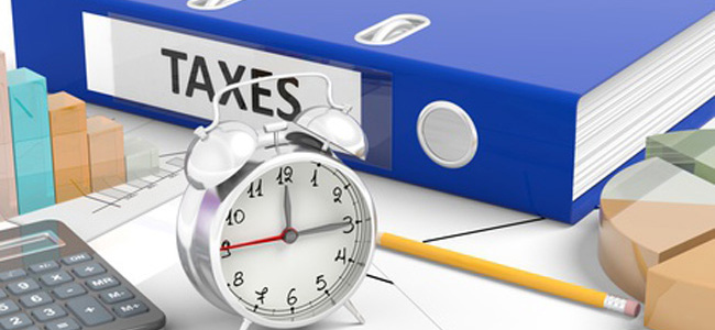 Clock with”Taxes” folder on busy office desk.